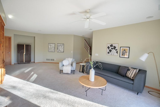 living room with light carpet, visible vents, baseboards, ceiling fan, and stairs