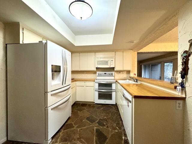 kitchen with stone floors, a sink, white appliances, a peninsula, and butcher block counters