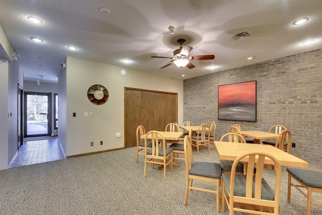 dining room featuring a ceiling fan, a textured ceiling, brick wall, visible vents, and baseboards