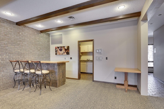 bar with a textured ceiling, brick wall, beamed ceiling, visible vents, and a bar