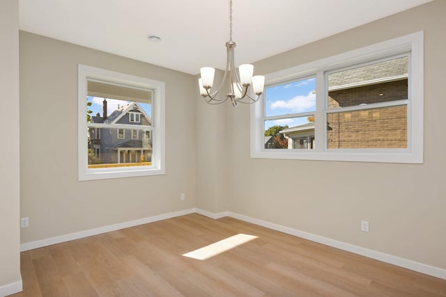 empty room with a chandelier, light hardwood / wood-style flooring, and a wealth of natural light