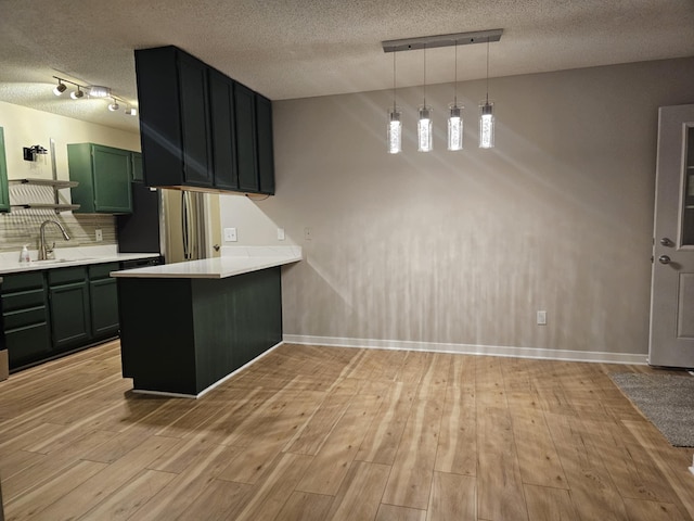 kitchen with kitchen peninsula, track lighting, sink, decorative light fixtures, and light hardwood / wood-style floors