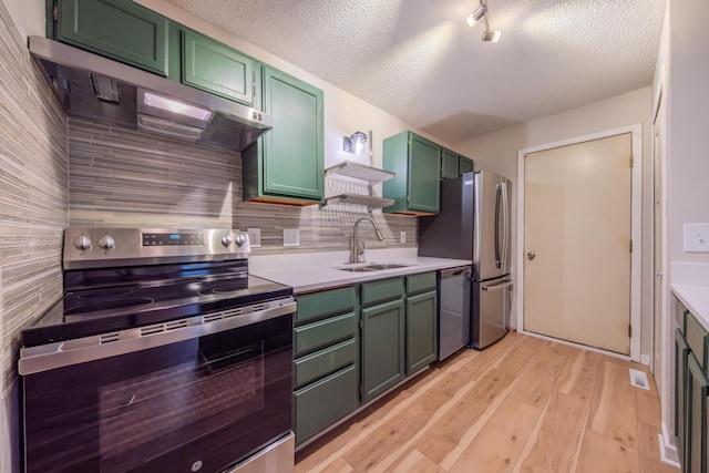 kitchen featuring sink, green cabinets, light hardwood / wood-style floors, decorative backsplash, and appliances with stainless steel finishes