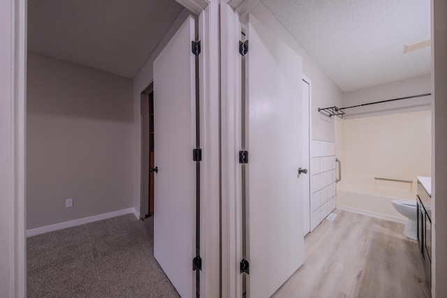 hall with a textured ceiling and light hardwood / wood-style flooring