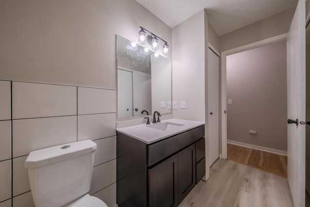 bathroom featuring wood-type flooring, vanity, toilet, and tile walls