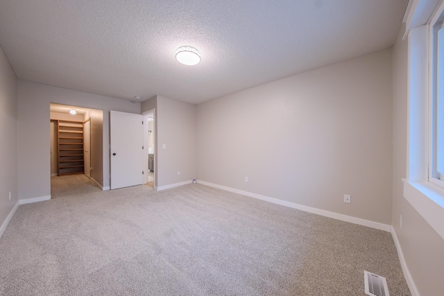 unfurnished bedroom with carpet, a textured ceiling, a spacious closet, and a closet