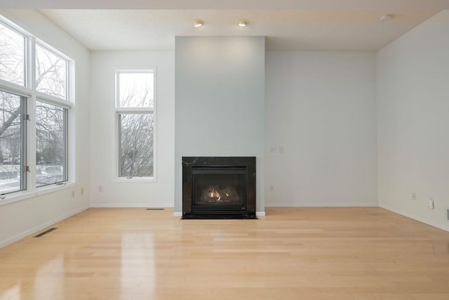 unfurnished living room with wood finished floors, a fireplace with flush hearth, visible vents, and baseboards