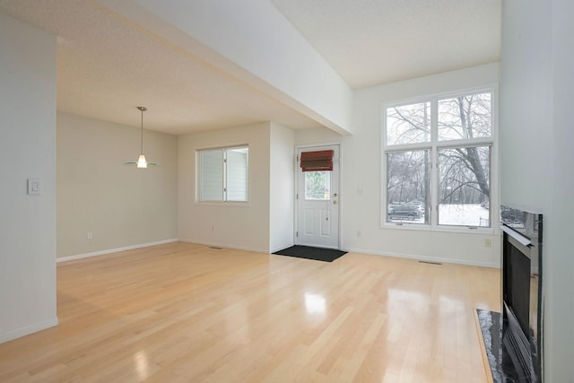 foyer entrance with light wood-type flooring, a fireplace with flush hearth, and baseboards