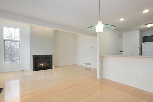 unfurnished living room with light wood-style floors, visible vents, a textured ceiling, and a glass covered fireplace