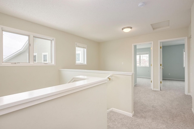 corridor featuring light carpet, baseboards, an upstairs landing, and attic access