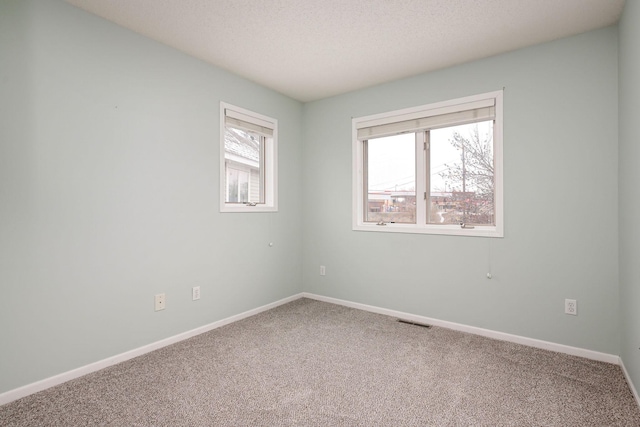 carpeted spare room with visible vents, a textured ceiling, and baseboards