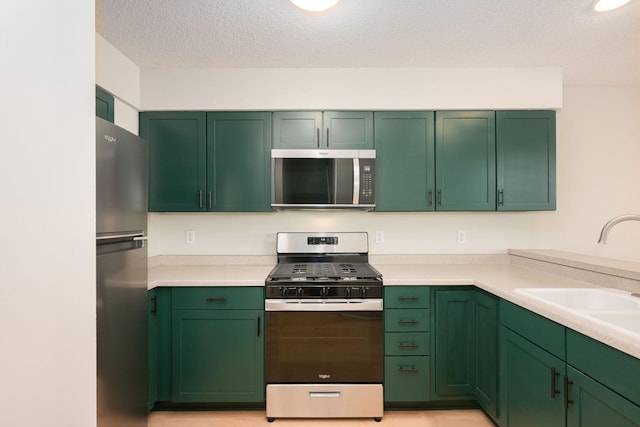 kitchen with a textured ceiling, light countertops, appliances with stainless steel finishes, and a sink