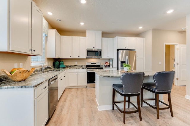 kitchen with appliances with stainless steel finishes, light wood-type flooring, sink, a center island, and white cabinetry