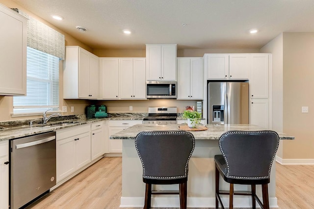 kitchen featuring light stone countertops, light wood-type flooring, stainless steel appliances, sink, and a center island