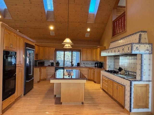 kitchen with a center island, hanging light fixtures, backsplash, black appliances, and light wood-type flooring