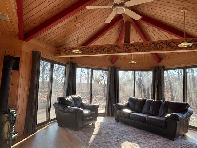 sunroom with wood ceiling, vaulted ceiling with beams, a wood stove, and a wealth of natural light