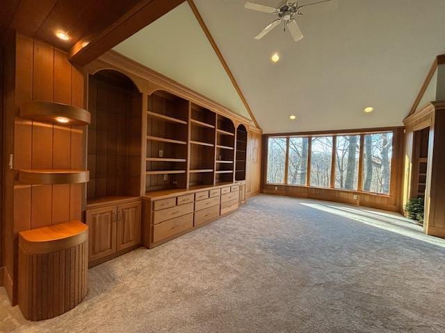 unfurnished living room with lofted ceiling with beams, light colored carpet, ceiling fan, and wood walls