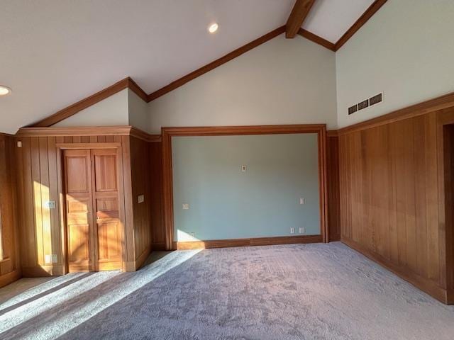 unfurnished living room featuring lofted ceiling with beams, wood walls, and light carpet