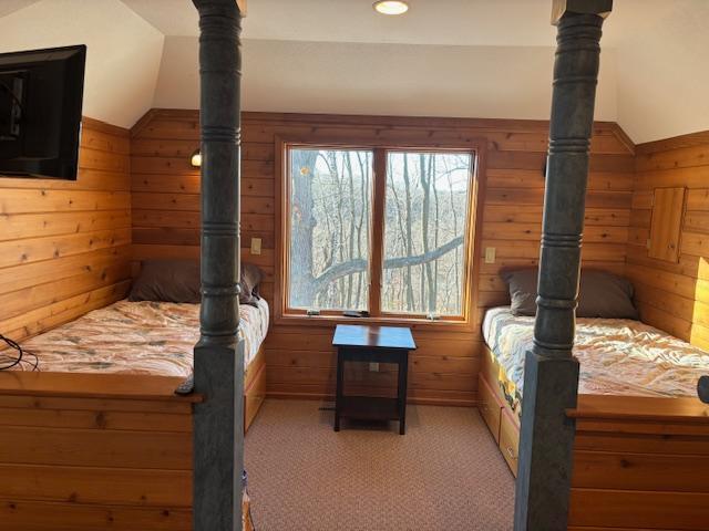 carpeted bedroom featuring wooden walls and vaulted ceiling