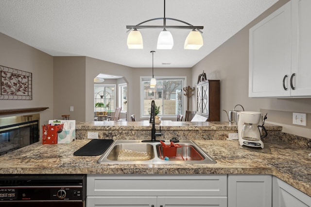 kitchen featuring dishwasher, sink, white cabinets, and decorative light fixtures