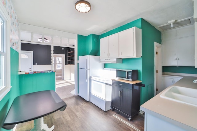 kitchen featuring stove, sink, hardwood / wood-style flooring, white fridge, and white cabinetry