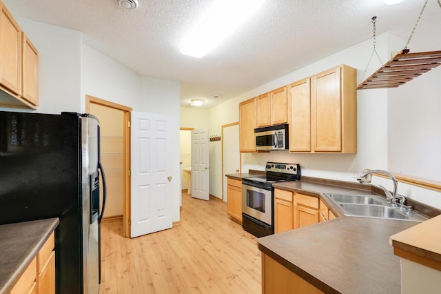 kitchen featuring light brown cabinetry, light wood-type flooring, a textured ceiling, stainless steel appliances, and sink