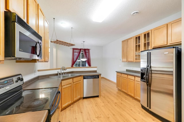 kitchen featuring appliances with stainless steel finishes, light wood-type flooring, a textured ceiling, sink, and pendant lighting