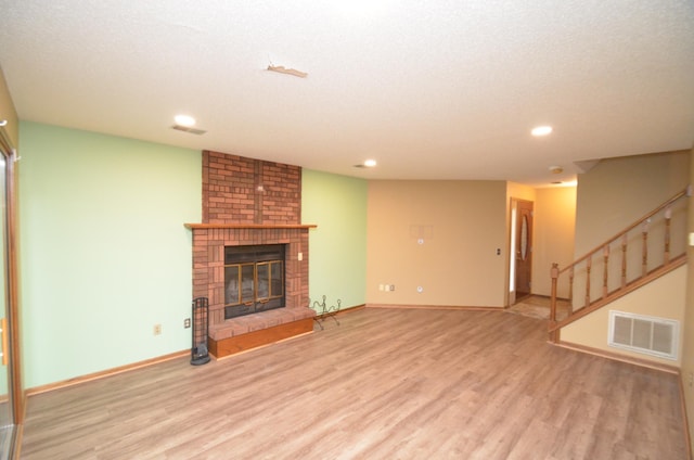 unfurnished living room with a textured ceiling, light hardwood / wood-style floors, and a brick fireplace