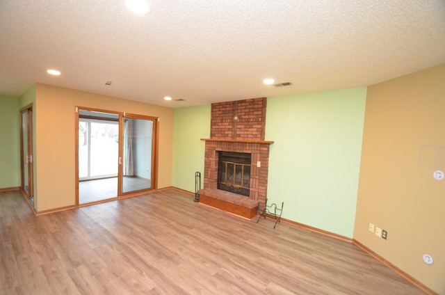 unfurnished living room with a brick fireplace, a textured ceiling, and light hardwood / wood-style flooring