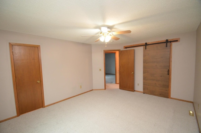 unfurnished bedroom featuring a textured ceiling, a barn door, carpet floors, and ceiling fan