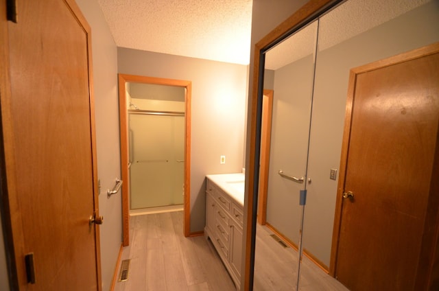 bathroom featuring a shower with shower door, vanity, wood-type flooring, and a textured ceiling