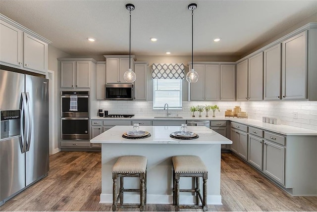 kitchen with sink, hanging light fixtures, appliances with stainless steel finishes, a kitchen island, and dark hardwood / wood-style flooring