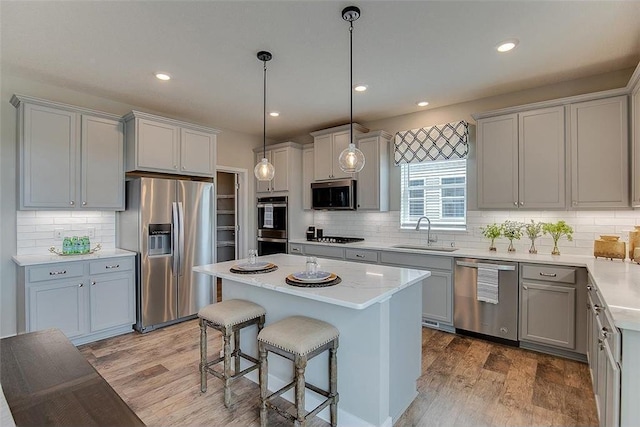 kitchen featuring appliances with stainless steel finishes, sink, pendant lighting, light hardwood / wood-style floors, and a kitchen island