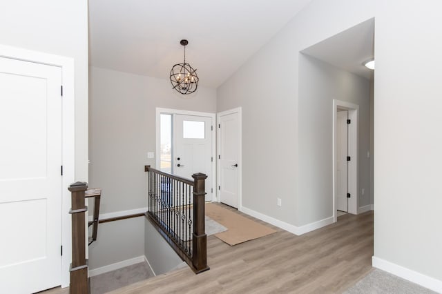 foyer entrance with light hardwood / wood-style floors, vaulted ceiling, and a notable chandelier