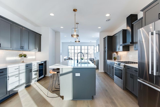 kitchen featuring appliances with stainless steel finishes, sink, wall chimney range hood, pendant lighting, and a center island with sink