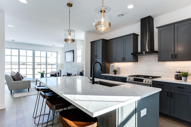 kitchen featuring a kitchen island with sink, wall chimney range hood, sink, decorative light fixtures, and dark hardwood / wood-style flooring