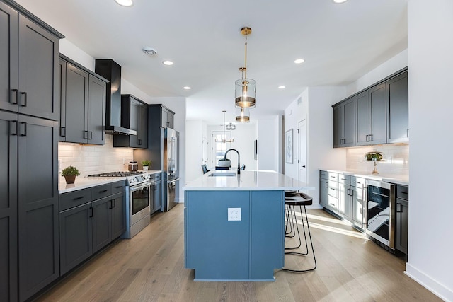 kitchen featuring high end appliances, a center island with sink, wall chimney range hood, sink, and light hardwood / wood-style flooring