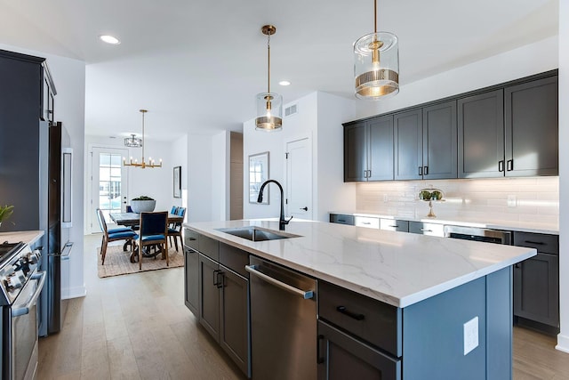 kitchen with high quality appliances, a center island with sink, sink, hanging light fixtures, and light hardwood / wood-style floors