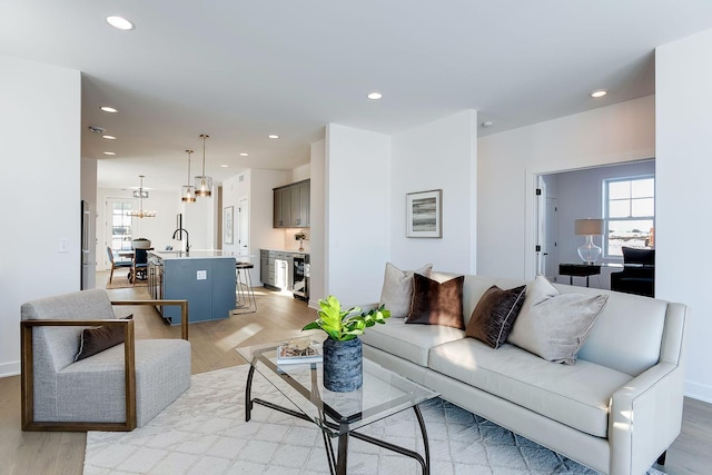 living room featuring light wood-type flooring, an inviting chandelier, and sink