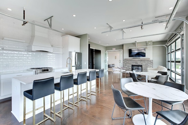 kitchen with a breakfast bar, a center island with sink, decorative backsplash, white cabinetry, and stainless steel appliances