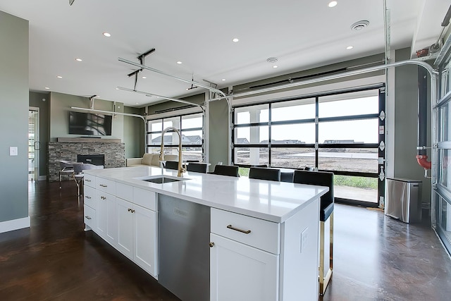 kitchen with dishwasher, sink, a fireplace, white cabinets, and a center island with sink