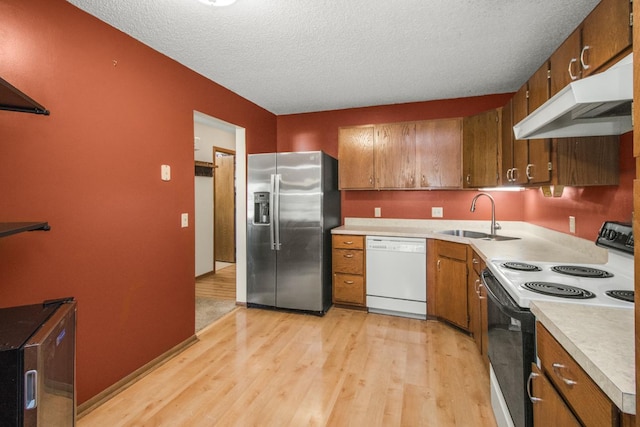 kitchen with light wood-type flooring, a textured ceiling, white appliances, and sink