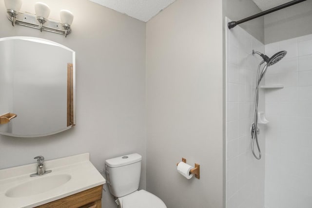 bathroom with vanity, toilet, tiled shower, and a textured ceiling