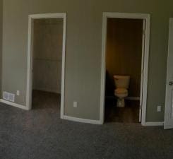 unfurnished bedroom with dark colored carpet, ensuite bathroom, a spacious closet, and a closet