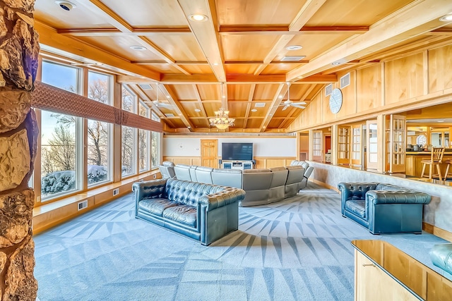 living room with light colored carpet, wooden walls, beamed ceiling, and ceiling fan with notable chandelier