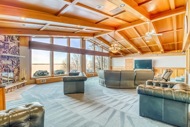 carpeted living room with ceiling fan with notable chandelier, a stone fireplace, and vaulted ceiling with beams