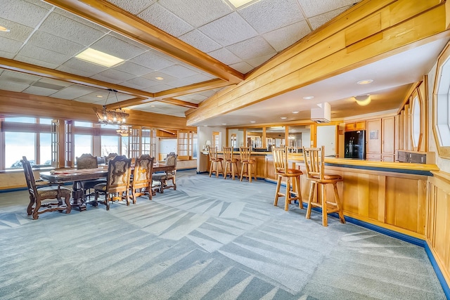 dining room featuring light carpet, a paneled ceiling, and wood walls