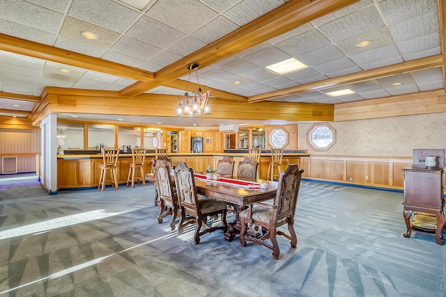 dining area featuring a notable chandelier, beamed ceiling, wood walls, and dark carpet