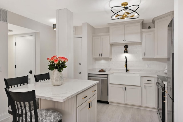 kitchen with decorative backsplash, a kitchen breakfast bar, stainless steel appliances, sink, and light hardwood / wood-style floors