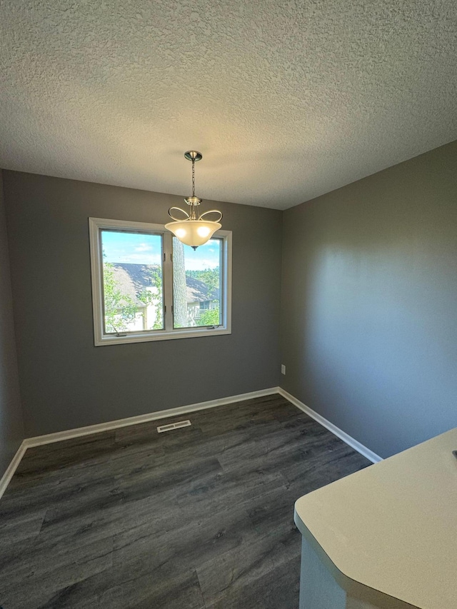 unfurnished dining area featuring a textured ceiling, dark hardwood / wood-style flooring, and an inviting chandelier